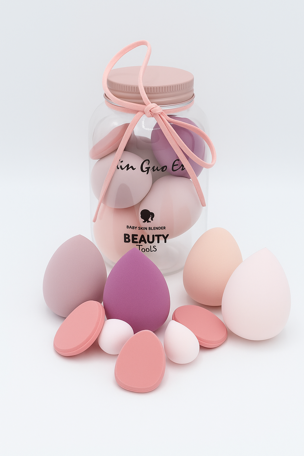 Frasco transparente con esponjas de maquillaje Coperma en tonos pastel y lazo rosa decorativo.