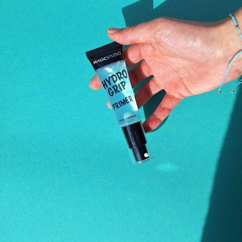prebase Magic Studio Hydro Grip Primer sostenida en mano fondo azul