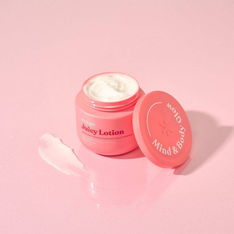 loción corporal Juicy Flor de Mayo textura cremosa hidratante sobre fondo rosa
