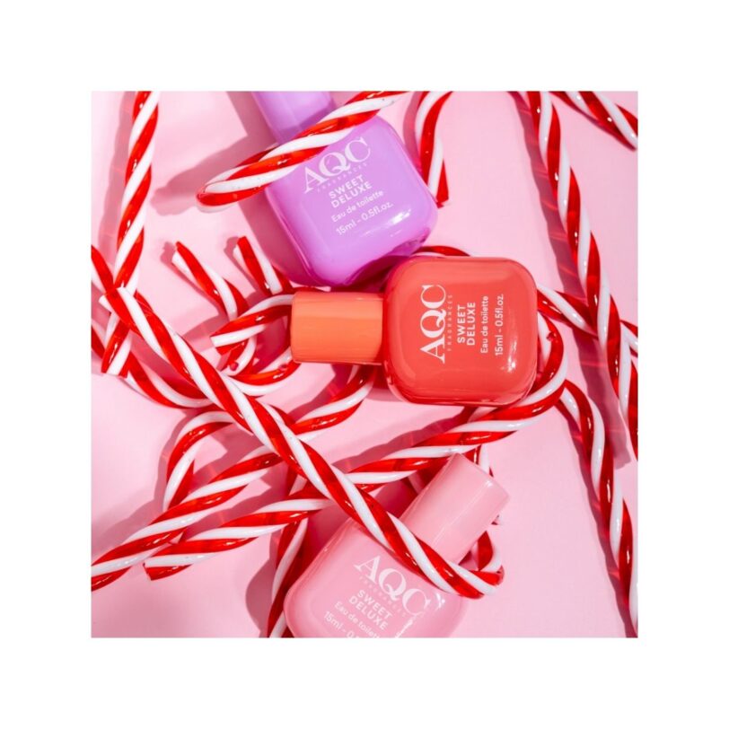 Colección AQC Sweet Luxe con tres eau de toilette en tonos pastel sobre un fondo rosa decorado con bastones de caramelo.