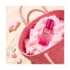 Frasco de Hair & Body Mist Sweet Cloud de Flor de Mayo dentro de un bolso de rafia rosa con algodón de azúcar sobre arena de playa
